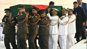 একটি কফিনের পাশে পুরো বাংলাদেশ এ এক মহাকাব্যিক প্রস্থান। দেশের কোটি মানুষের হৃদস্পন্দন বিএনপি চেয়ারপারসন ও তিনবারের সাবেক প্রধানমন্ত্রী খালেদা জিয়ার জানাজায় ৩১ ডিসেম্বর রাজধানী ঢাকা এক নজিরবিহীন জনসমুদ্রে পরিণত হয়েছিল। এই জানাজায় জনসমুদ্র শব্দটিও যেন বিশালতার কাছে হার মানে। সকালের কুয়াশাচ্ছন্ন সূর্য ওঠার আগেই দেশের প্রতিটি প্রান্ত-টেকনাফের নাফ নদী থেকে শুরু করে তেঁতুলিয়ার বাংলাবান্ধা পর্যন্ত-প্রতিটি জনপদ থেকে আসা মানুষের অন্তহীন স্রোত ঢাকার প্রতিটি প্রবেশপথ ও মহাসড়ককে কার্যত অচল করে দেয়। বিকেল ৩টায় যখন জাতীয় সংসদ ভবনের দক্ষিণ প্লাজায় খালেদা জিয়ার জানাজা শুরু হয়, তখন মানিক মিয়া এভিনিউয়ের আশেপাশের সড়কগুলো কার্যত স্থবির হয়ে পড়ে। জাতীয় সংসদ ভবনের দক্ষিণ প্লাজা থেকে কয়েক বর্গকিলোমিটার এলাকা জুড়ে কেবল মানুষের মাথা আর শোকাতুর মুখচ্ছবি চোখে পড়ছিল। মানিক মিয়া এভিনিউ ছাপিয়ে জনস্রোত আছড়ে পড়ে আশেপাশের কয়েক কিলোমিটার জুড়ে। জানাজাস্থল মানিক মিয়া এভিনিউ পূর্ণ হয়ে মানুষের ভিড় ছড়িয়ে পড়ে উত্তরে জাহাঙ্গীর গেট, পশ্চিমে মিরপুর রোড এবং পূর্বে ফার্মগেট পেরিয়ে কারওয়ান বাজার, বাংলামোটর ও মগবাজার পর্যন্ত। মাইকের আওয়াজ যতদূর পৌঁছিয়েছে, মানুষ ততদূরেই রাস্তায় কাতারবন্দি হয়ে দাঁড়িয়েছিলেন। যেদিকে চোখ গিয়েছে সেদিকেই কেবল চোখে পড়েছে মানুষের ঢল। কোথাও তিল ধারণের ঠাঁই ছিল না। কেউ বাসায়, কেউবা ফুটওভার ব্রিজে-যে যেখানে জায়গা পেয়েছেন জানাজায় দাঁড়িয়ে গেছেন। শুধু বিএনপির নেতাকর্মী নন, সাধারণ মানুষ, চাকরিজীবী, শিক্ষক-শিক্ষার্থী, রিকশাচালক থেকে শুরু করে দেশের সর্বস্তরের মানুষ জানাজায় অংশ নেন। সংসদ ভবন এলাকার গাছ, ফুটপাত, এমনকি নিকটস্থ ভবনগুলোর ছাদও ছিল লোকে লোকারণ্য। শোনা গেছে লাখো কণ্ঠের কান্নাজড়িত দোয়া। অনেকের চোখের কোণে ছিল জল, কেউবা হাত তুলে নীরবে দোয়া করেছেন। রাজনৈতিক বিশেষজ্ঞ ও পর্যবেক্ষকদের মতে, এটি ছিল বাংলাদেশের ইতিহাসে স্মরণকালের বৃহত্তম জানাজা, যেখানে মানুষের উপস্থিতি কেবল সংখ্যা দিয়ে পরিমাপ করা ছিল এক অসম্ভব প্রয়াস। কফিন যখন শুভ্র ফুলের চাদরে আবৃত হয়ে জানাজার মঞ্চের দিকে আনা হচ্ছিলো, তখন গগনবিদারী ক্রন্দন আর ‘আল্লাহু আকবর’ ধ্বনিতে পুরো এলাকা এক অপার্থিব ও আধ্যাত্মিক আবহের সৃষ্টি করে। উপস্থিত অগণিত মানুষের প্রতিটি অশ্রুবিন্দু যেন তার দীর্ঘ সংগ্রামের প্রতি এক একটি জীবন্ত সাক্ষ্য দিচ্ছিলো। রাষ্ট্রীয় সম্মাননার অংশ হিসেবে যখন সশস্ত্র বাহিনীর সুসজ্জিত চৌকস দল খালেদা জিয়াকে শেষবারের মতো গার্ড অব অনার প্রদান করছিল, তখন বিউগলের সেই করুণ সুর প্রতিটি নাগরিকের হৃদয়ে তীরের মতো বিঁধছিল, যা উপস্থিত লক্ষ লক্ষ মানুষকে অশ্রুভেজা চোখে স্তব্ধ করে দেয়। আশির দশকের উত্তাল রাজপথ থেকে শুরু করে সেনাশাসকের পতন ঘটানো, সংসদীয় গণতন্ত্রের পুনরুত্থান এবং আধুনিক বাংলাদেশ বিনির্মাণে খালেদা জিয়ার যে অনবদ্য ও কালজয়ী ভূমিকা, তার শেষ বিদায়ে মানুষ তা পরম শ্রদ্ধায় ও বেদনার্ত হৃদয়ে স্মরণ করছিল। ইতিহাসের সাক্ষী হয়ে থাকা এই জনপদ এর আগে কবে এমন স্বতঃস্ফূর্ত ও বাঁধভাঙা মানুষের ঢল দেখেছিল, তা নিয়ে প্রবীণরাও বিস্ময় প্রকাশ করেছেন। এটি কেবল একটি জানাজা ছিল না, বরং ছিল একজন কিংবদন্তি নেত্রীর প্রতি এদেশের আপামর জনতার অকৃত্রিম ভালোবাসা, গভীর কৃতজ্ঞতা ও এক ঐতিহাসিক নীরব প্রতিবাদের স্মারক। দলমত-নির্বিশেষে শোকার্ত মানুষের এই ঢল প্রমাণ করেছে, রাজনীতির ‘আপোসহীন নেত্রী’ খালেদা জিয়া মানুষের হৃদয়ে কতটা গভীরে স্থান করে নিয়েছিলেন। প্রবীণ রাজনৈতিক বিশ্লেষক থেকে শুরু করে সাধারণ মানুষ, সবাই একবাক্যে স্বীকার করছেন, ‘দেশে এমন জানাজা এর আগে আর দেখেনি কেউ।’ জাতীয় সংসদ ভবনের দক্ষিণ প্লাজায় মূল জানাজার সঙ্গে মিল রেখে একই সময়ে দেশের বিভিন্ন স্থানেও গায়েবানা জানাজা অনুষ্ঠিত হয়। এসব গায়েবানা জানাজায়ও হাজার হাজার মানুষ অংশ নেন। শুধু দেশে নয়, চীনেও খালেদা জিয়ার গায়েবানা জানাজা অনুষ্ঠিত হয়। দীর্ঘ রোগভোগ, কারাবাস আর নানা চড়াই উৎরাইয়ের পর তার খালেদা জিয়ার এই বিদায় প্রমাণ করে, ক্ষমতার বাইরে থেকেও একজন নেতা কীভাবে গণমানুষের মনে বেঁচে থাকতে পারেন। জাতীয় সংসদ ভবনে জানাজা শেষে যখন কফিনবাহী গাড়িটি শেরেবাংলা নগরের দিকে ধীরলয়ে যাত্রা শুরু করে, তখন ঢাকার রাজপথের দৃশ্য ছিল বর্ণনাতীত। রাস্তার দুই ধারের সুউচ্চ অট্টালিকার বারান্দা থেকে শুরু করে ফুটপাথ, গাছের ডাল কিংবা ল্যাম্পপোস্ট-কোথাও তিল ধারণের ঠাঁই ছিল না। হাজার হাজার মানুষ মুঠো মুঠো ফুলের পাপড়ি ছিটিয়ে তাঁদের প্রিয় ‘দেশনেত্রী’ ও ‘মাদার অফ ডেমোক্রেসি’কে শেষ বিদায়ের অভিবাদন জানান। অনেকে প্রিয় নেত্রীর কফিনটি একবার ছুঁয়ে দেখার জন্য ব্যারিকেড ভেঙে এগিয়ে আসার চেষ্টা করেন, তাদের চোখে-মুখে ছিল এক আপনজনকে হারানোর তীব্র হাহাকার। দীর্ঘ কয়েক দশকের বিরহ, একাকী সংগ্রাম এবং শোকগাথা পেরিয়ে খালেদা জিয়া আবার ফিরে গেলেন তার চিরকালের জীবনসঙ্গী ও আদর্শিক গুরু শহীদ জিয়াউর রহমানের পাশে। স্বামীর কবরের পাশেই তার এই অন্তিম শয়ান যেন এক ঐতিহাসিক ও শাশ্বত পুনর্মিলন, যা বাংলার রাজনীতির ইতিহাসে এক অমর কাব্য হয়ে চিরকাল অম্লান থাকবে। আওয়ামী লীগের দীর্ঘ ১৬ বছরের শাসনামলে দীর্ঘদিন নির্যাতনের শিকার হয়েছিলেন বিএনপি চেয়ারপারসন খালেদা জিয়া।খালেদা জিয়া, করেছেন কারাভোগ। চিকিৎসার সুযোগও দেওয়া হয়নি তাকে। ফলে ধীরে ধীরে হৃদরোগ, ডায়াবেটিস, আর্থ্রাইটিস, লিভার সিরোসিস, কিডনির জটিলতাসহ নানা শারীরিক অসুস্থতা দেখা দেয় খালেদা জিয়ার। ছাত্র-জনতার গণঅভ্যুত্থানে ২০২৪ সালের ৫ আগস্ট আওয়ামী সরকারের পতনের পরদিন ৮০ বছর বয়সী খালেদা জিয়াকে মুক্তি দেন রাষ্ট্রপতি। এরপর উন্নত চিকিৎসার জন্য ২০২৫ সালের ৭ জানুয়ারি লন্ডনে যান খালেদা জিয়া। ১১৭ দিন লন্ডনে চিকিৎসা শেষে ৬ মে তিনি দেশে ফেরেন। এরপর শারীরিক নানা জটিলতায় সাবেক এই প্রধানমন্ত্রীকে একাধিকবার হাসপাতালে যেতে হয়েছে। রাজধানীর এভারকেয়ার হাসপাতালে ৩৭ দিন ধরে মৃত্যুর সঙ্গে পাঞ্জা লড়ে ৩০ ডিসেম্বর সকাল ৬টায় মৃত্যুবরণ করেন তিনি। মৃত্যুকালে তার বয়স হয়েছিল ৮০ বছর।